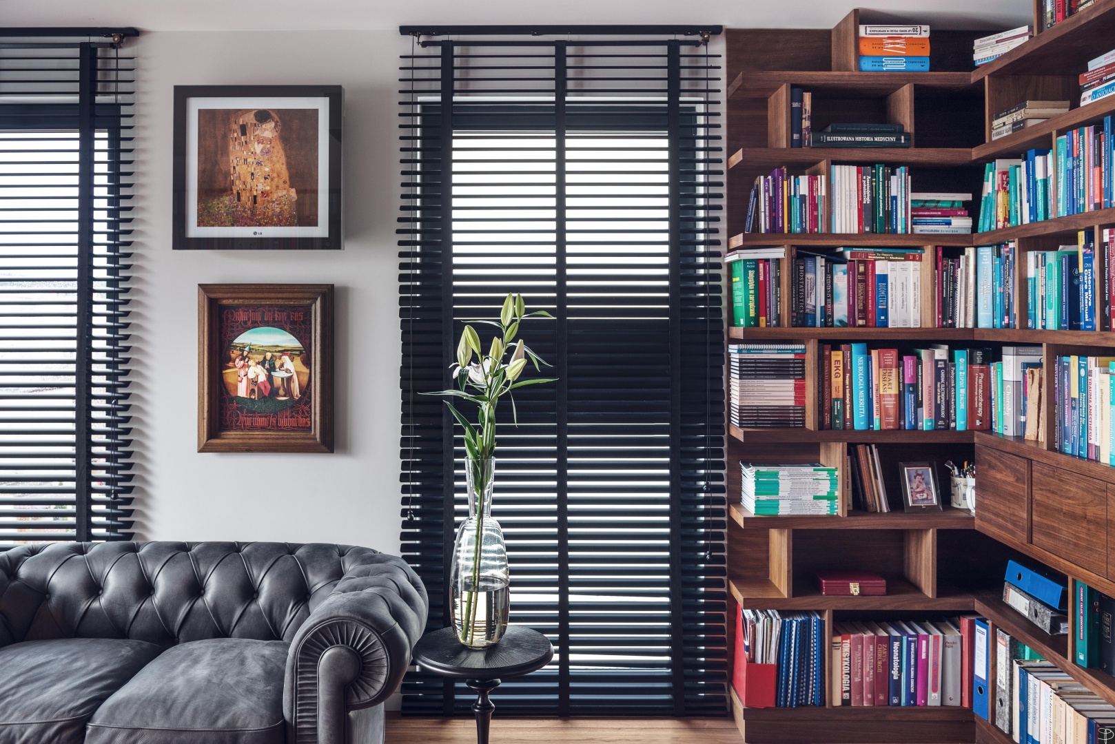 Klasycznego charakteru gabinetowi nadają ciężkie, czarne żaluzje, sofa w stylu chesterfield oraz klasyczny perski dywan, a nowoczesności - lekkie biurko, kolorowe krzesło oraz minimalistyczne lampy biurkowe. Fot. Tomirri Photography
