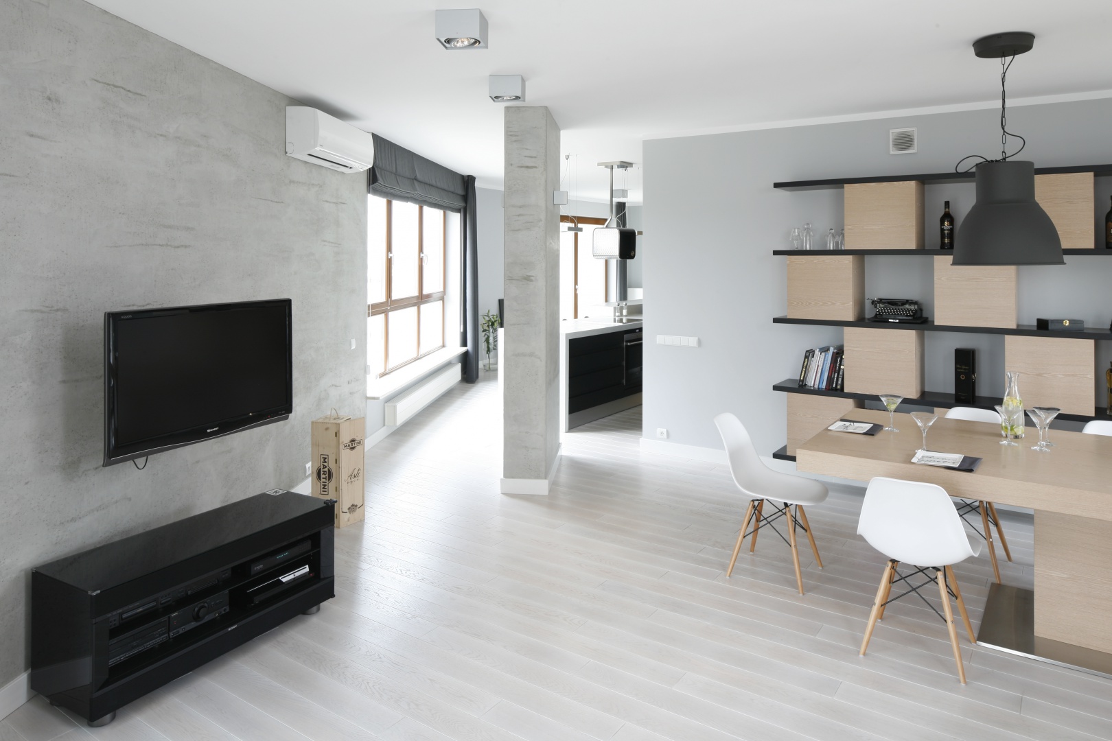Na ścianie za TV oraz dalej, na kolumnie sąsiadującej z kuchnią położono betonową strukturę, która podkreśla surowy charakter minimalistycznej aranżacji salonu. Projekt: Maciejka Peszyńska-Drews. Fot. Bartosz Jarosz